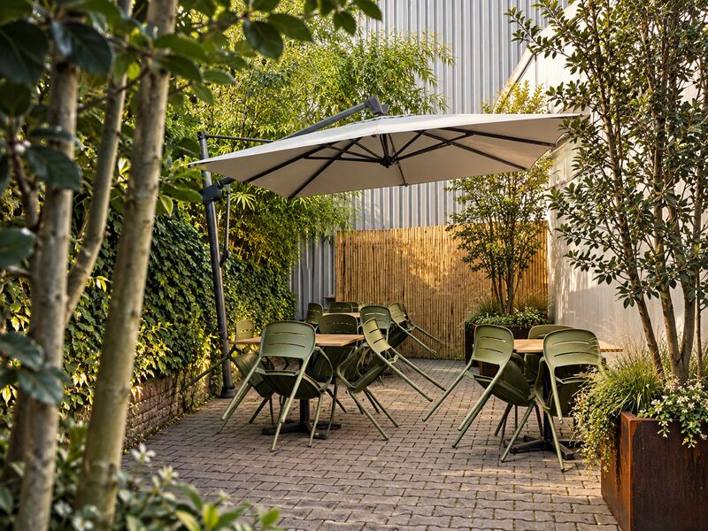 Hof mit Sonnenschirm, grünen Stühlen, Pflasterfläche und Bambus