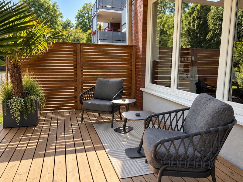 Holzdeck mit Lamellenwand, Loungesesseln und bepflanzten Gefäßen